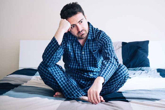 man sitting on his bed in pajamas thinking about a lot of things - insomnia - burnout