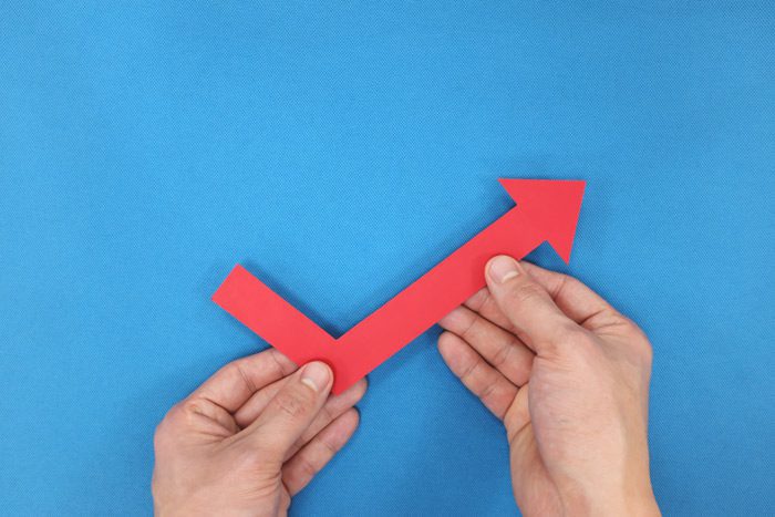 hands holding a red arrow that bends and travels upward on a bright blue background - bouncebackability