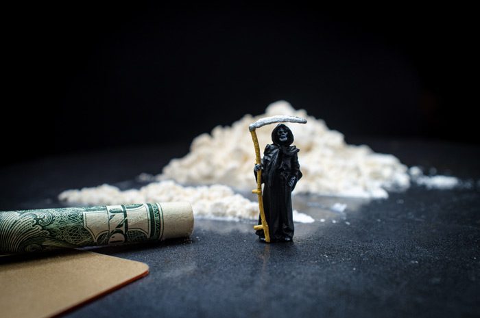 pile of cocaine with tiny grim reaper figurine standing in front of it