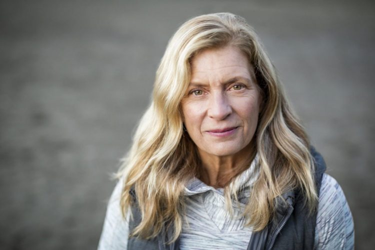 Headshot of mature woman with blond hair and in her 60’s with blurred background.